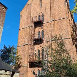 Brandladder met kooi en toegangsbalkons voor raamuitgang op een historisch bakstenen gebouw.