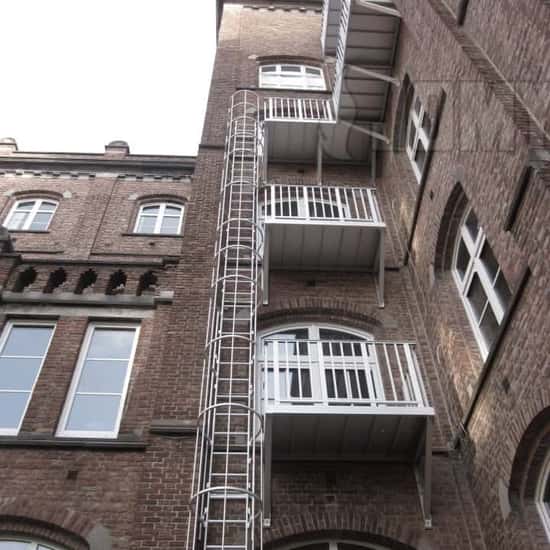 Veilige toegang tot een kooiladder via een toegangsbalkon op elke verdieping