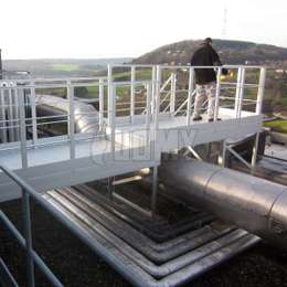Aluminium gangpad op een plat dak en gebruikt voor het oversteken van een pijp naar een metalen trap.